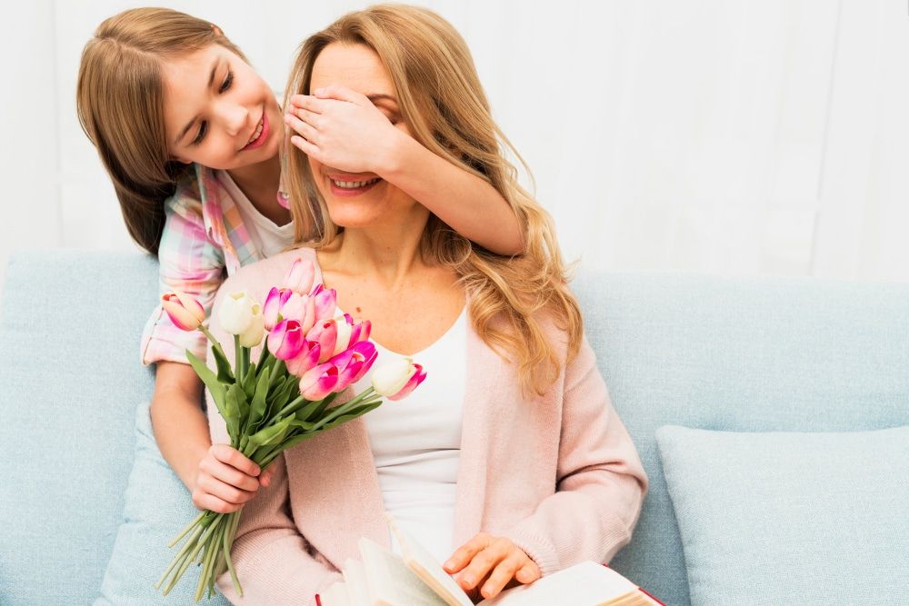 daughter closing eyes mother and giving surprised flowers