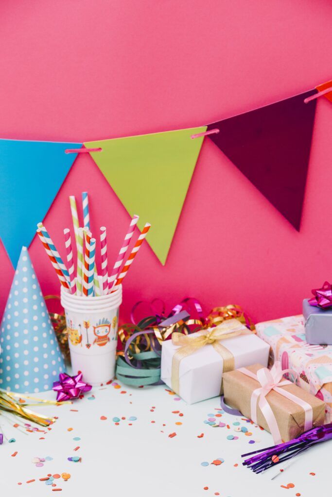 wrapped gift boxes party hat streamers ribbon bows buntings against pink background